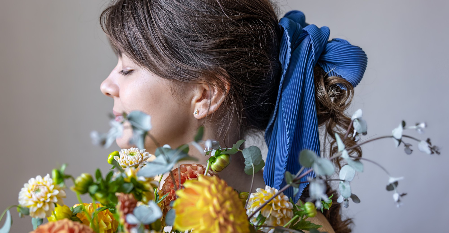 Une jeune femme tient un bouquet de fleurs dans ses mains et porte un accessoire de cheveux en tissu